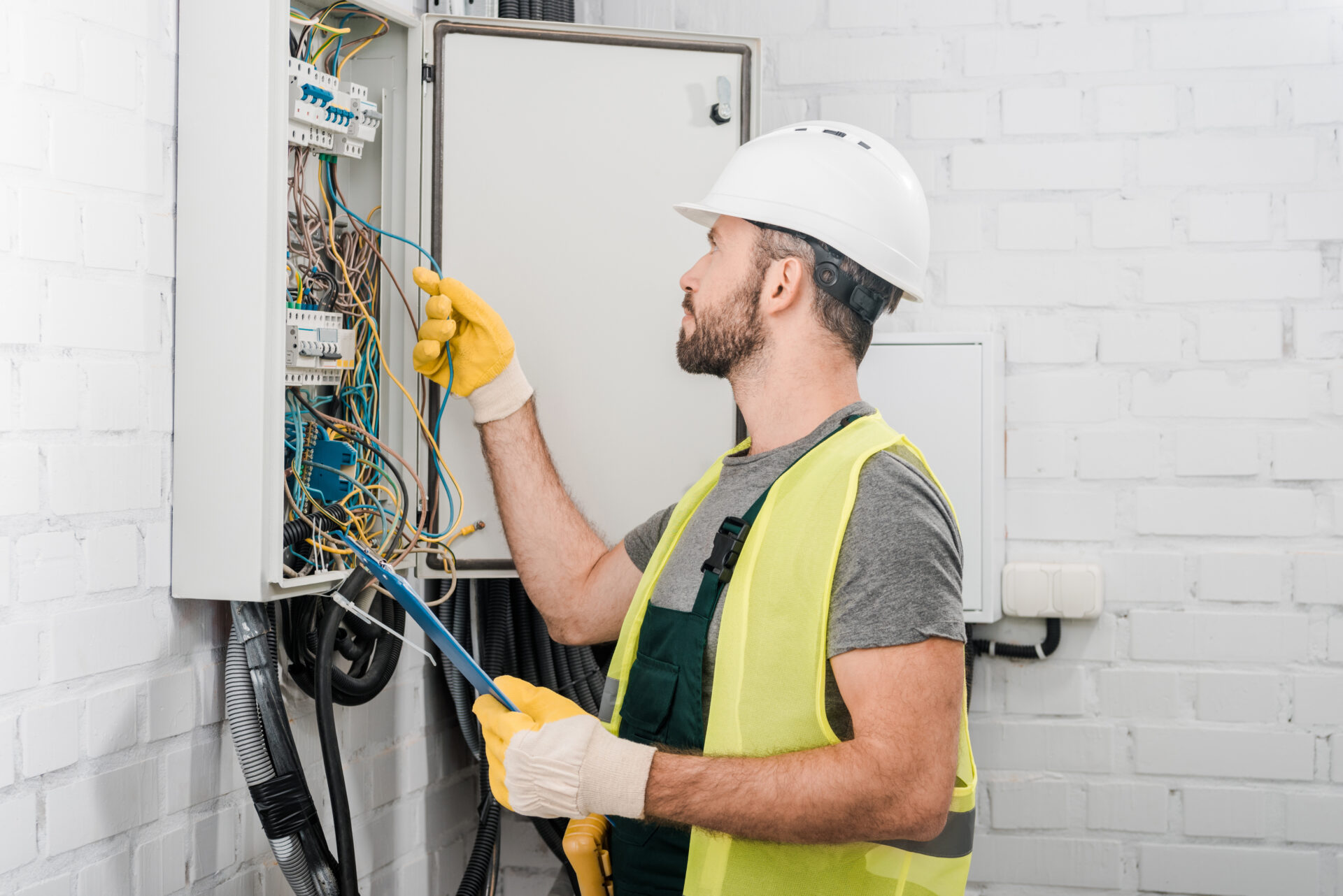 side view of electrician holding clipboard and checking wires in side view of electrician holding clipboard and checking wires in