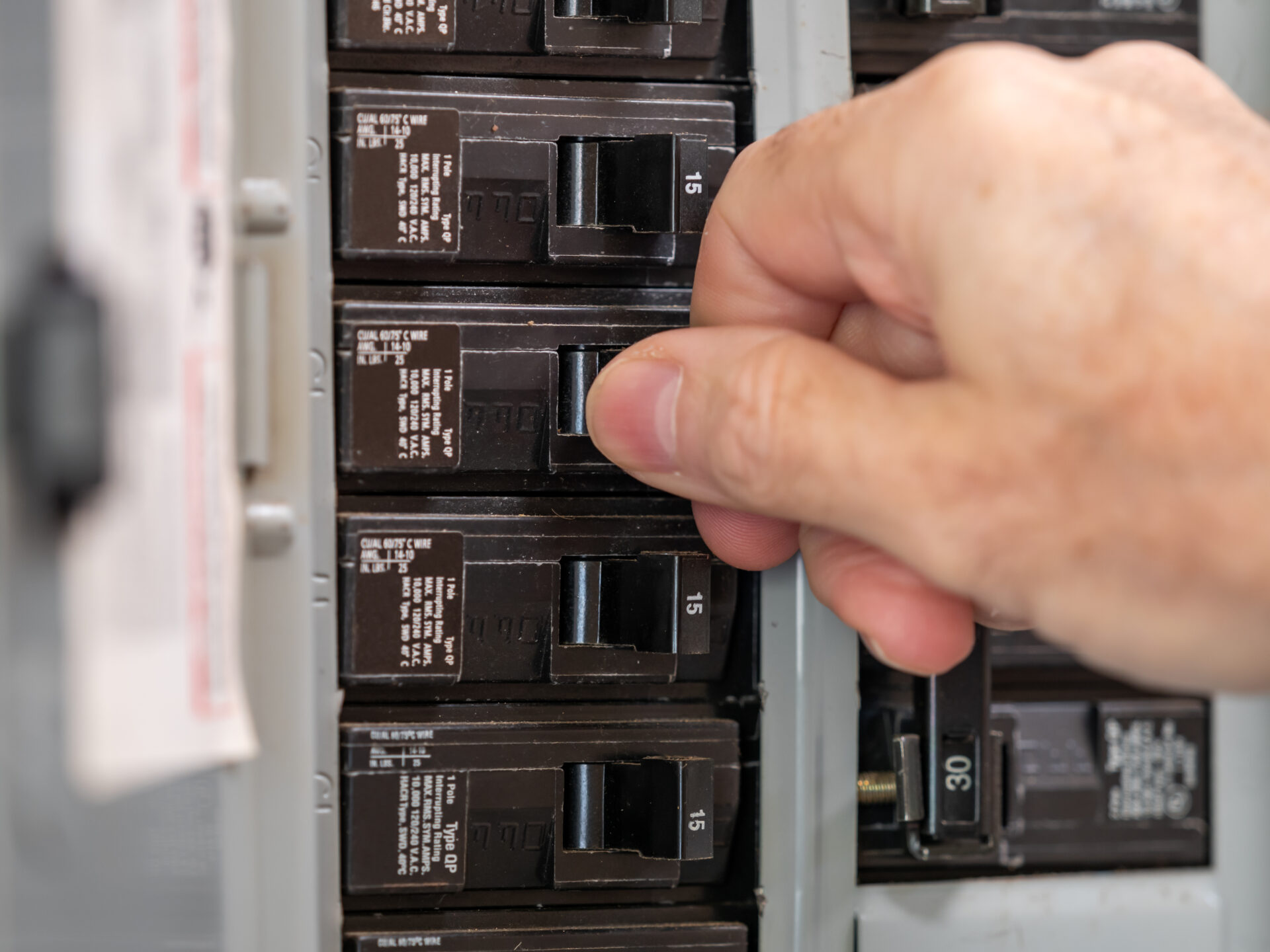 Male electrician turning off power for electrical outlet at circuit breaker box. Resetting tripped breaker in residential electricity power panel. Male electrician turning off power for electrical outlet at circuit breaker box. Resetting tripped breaker in residential electricity power panel.
